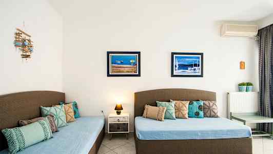 To senge med blå sengetæpper og dekorative puder, to billeder med maritime motiv på væggen. (AI-genereret tekst)