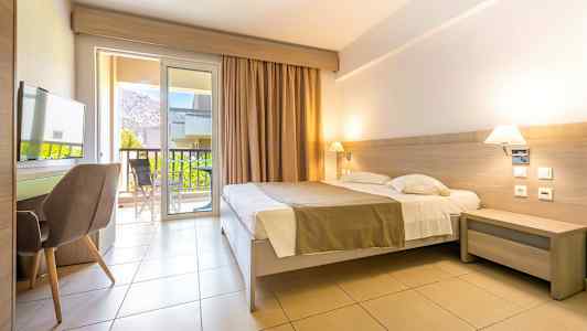 Et hotelværelse med dobbeltseng, skrivebord og stol. Altandøre leder ud til en altan med udsigt. (AI-genereret tekst)