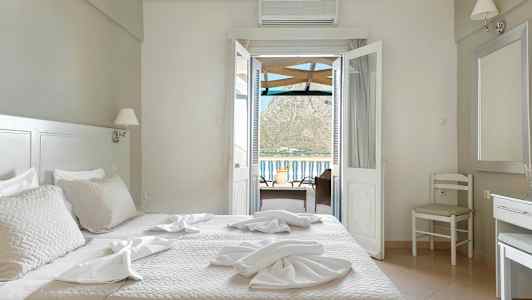 Et hotelværelse med en seng, stole og et bord med udsigt gennem dørene ud mod balkonen og bjergene i baggrunden. (AI-genereret tekst)