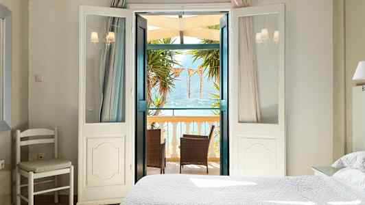 Et lyst soveværelse med åbne døre til en balkon med møbler og udsigt over havet. (AI-genereret tekst)