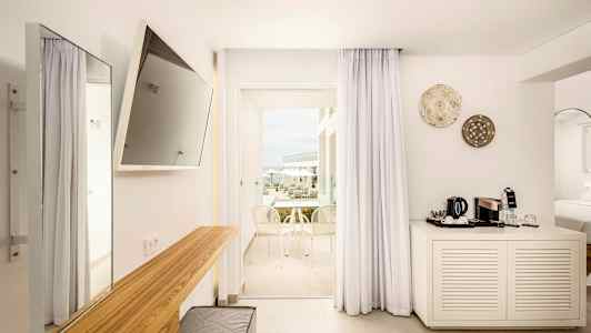 Et moderne hotelværelse med lys indretning, et tv på væggen, et skrivebord og en balkon med udsigt. (AI-genereret tekst)