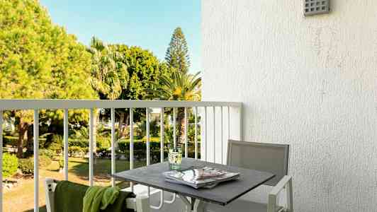 En altan med et bord og stole, med udsigt til en have med palmer. (AI-genereret tekst)