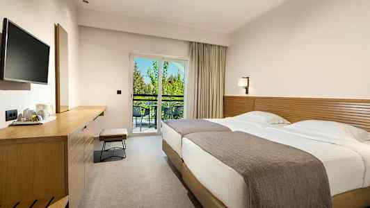 Et hotelværelse med to senge, en arbejdsbænk og en altan med udsigt. (AI-genereret tekst)