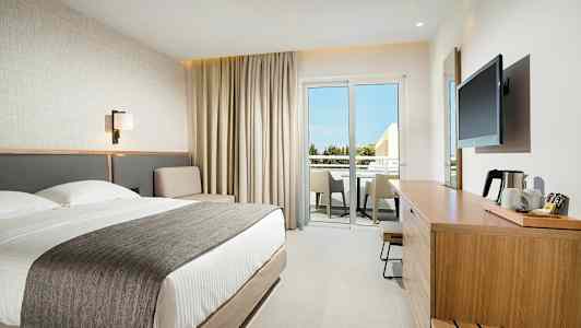 Moderne hotelværelse med dobbeltseng, siddeområde og møbleret altan. (AI-genereret tekst)