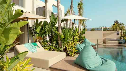 En pool omgivet af grønne planter og solmøbler. (AI-genereret tekst)