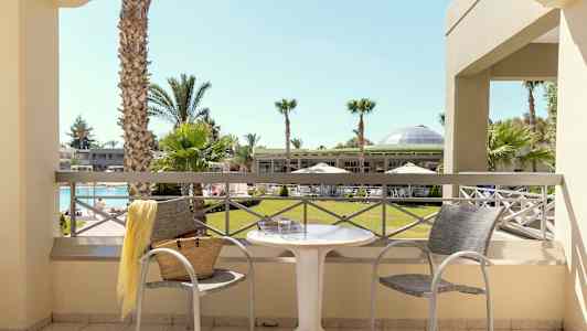 Udsigt fra altanen mod en have med palmer og en pool. (AI-genereret tekst)