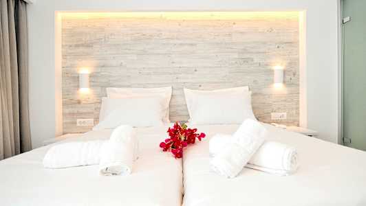 En hvid opredt dobbeltseng med røde blomster og foldede håndklæder på toppen. (AI-genereret tekst)