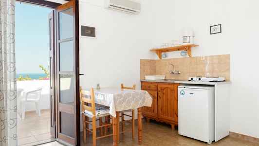 Et lille køkkenområde med bord, stole og en kogeplads. En dør fører ud til en terrasse med udsigt. (AI-genereret tekst)