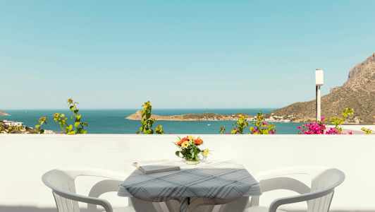 Udsigt over havet fra en balkon med et bord, to stole og en vase med blomster. (AI-genereret tekst)