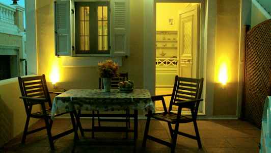 En terrasse med et bord og to stole, oplyst om aftenen, med en åbning mod et interiør. (AI-genereret tekst)