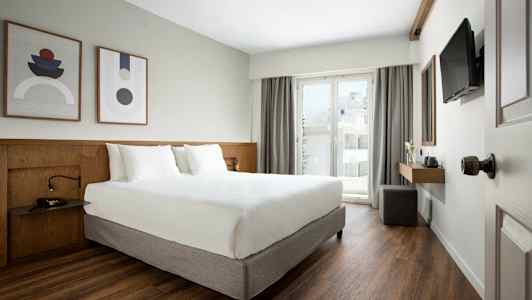 Moderne hotelværelse med dobbeltseng, kunst på væggen og altan med glasdør. (AI-genereret tekst)