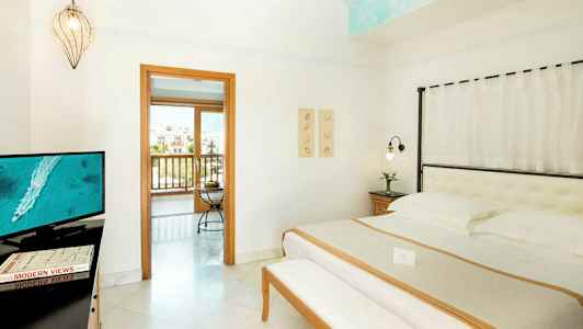 Interiør af et hotelværelse med en seng, et tv og en åbning til en balkon. (AI-genereret tekst)