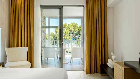 Hotelværelse med udsigt fra altan mod træer og hav. (AI-genereret tekst)