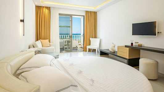 Interiør af et hotelværelse med en seng, siddepladser og en balkon med havudsigt. (AI-genereret tekst)