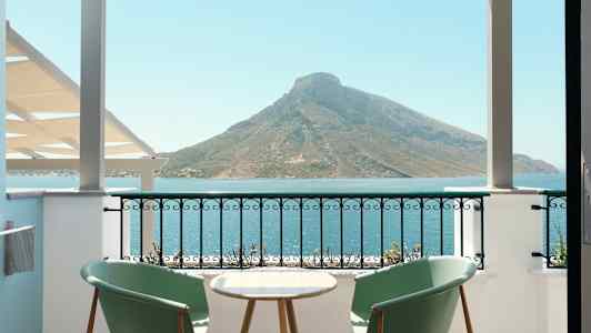 To stole og et bord på en altan med udsigt over havet og et bjerg. (AI-genereret tekst)