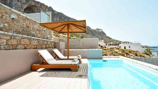 To liggestole under en parasol ved en pool med udsigt til kysten og bjerge. (AI-genereret tekst)