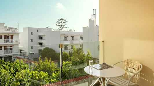 Altan med bord og stol, udsigt over hvide bygninger og grønne områder. (AI-genereret tekst)