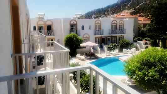 Hotelanlæg med en pool og liggestole omgivet af grønne planter. (AI-genereret tekst)