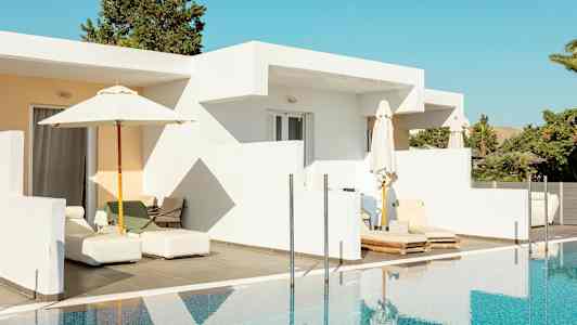 En hvid bygning med terrasse og solsenge ved en pool. (AI-genereret tekst)