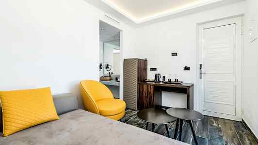 Et moderne hotelværelse med en gul lænestol, et sofabord, en sofa med en gul pude og en hvid dør. (AI-genereret tekst)