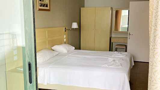 Billede af et hotelværelse med to enkeltsenge med hvidt sengetøj, et skab og et spejl. (AI-genereret tekst)