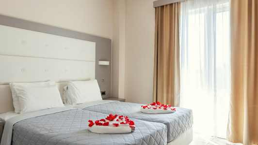 Et hotelværelse med to enkeltsenge dekoreret med røde rosenblade. (AI-genereret tekst)