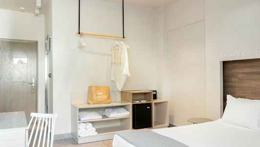 Et hotelværelse med en opredt seng, et garderobeområde og et bord med en stol. (AI-genereret tekst)