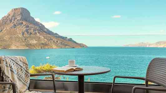 Et bord med en kop og en bog står på en balkon med udsigt over havet og et bjerg. (AI-genereret tekst)