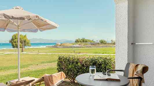 Udsigt fra terrasse med bord, stole, parasol og grønt område mod havet. (AI-genereret tekst)