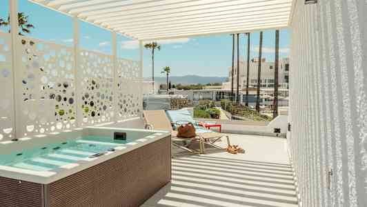 En terrasse med jacuzzi, liggestole og udsigt til palmer og bygninger i baggrunden. (AI-genereret tekst)