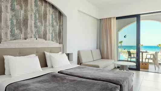 Hotelværelse med dobbeltsenge, et siddeområde og udsigt over havet gennem en glasdør. (AI-genereret tekst)