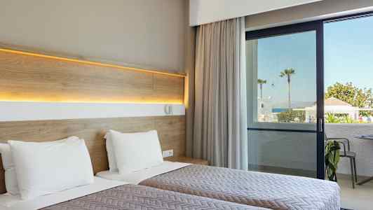 Hotelværelse med to enkeltsenge og udsigt til en terrasse og havet i baggrunden. (AI-genereret tekst)