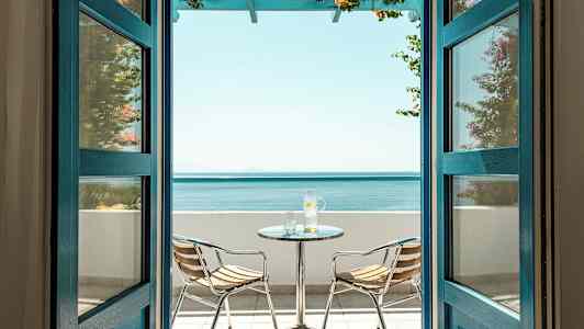 Udsigt gennem åbne døre til en terrasse med havudsigt, inklusive et bord og to stole. (AI-genereret tekst)