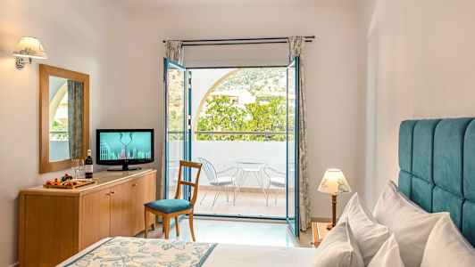 Et hotelværelse med en seng, en kommode med et TV og en altan med stole og bord. (AI-genereret tekst)