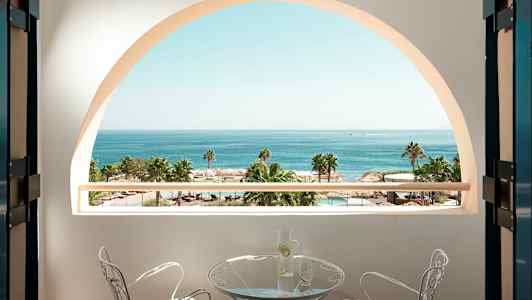 Udsigt fra en balkon med havet, palmer og en pool i baggrunden. (AI-genereret tekst)