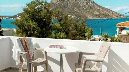 Udsigt fra en terrasse med to stole og et bord, mod havet og en klippe i baggrunden. (AI-genereret tekst)