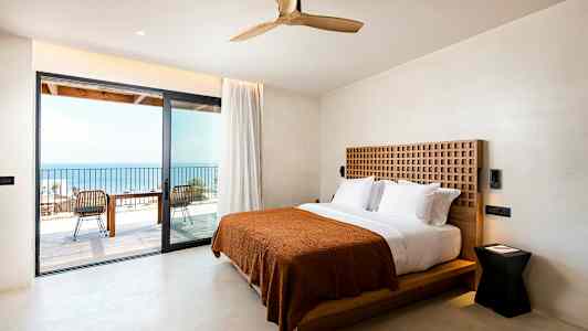 Hotelværelse med dobbeltseng og udgang til en altan med havudsigt. (AI-genereret tekst)