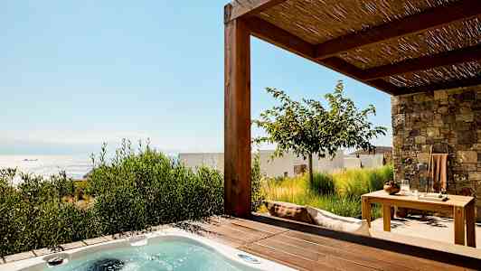 Billede af en terrasse med et spabad og havemøbler, havet er synligt i baggrunden. (AI-genereret tekst)