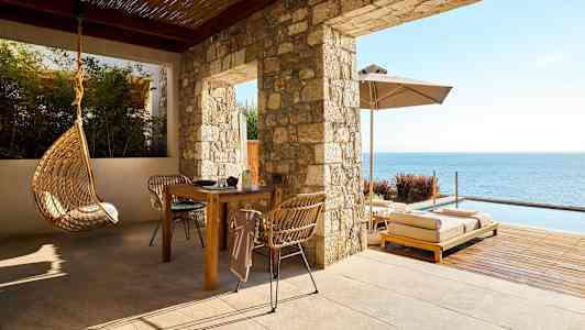 En terrasse med bord, stole, hængestol og solsenge ved havet. (AI-genereret tekst)