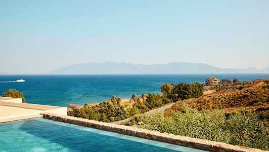 Udsigt over en pool, kysten og havet med en båd, der passerer. Bjergene ses i baggrunden. (AI-genereret tekst)