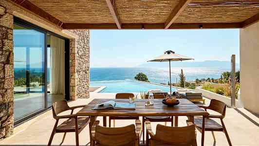 Udendørs veranda med træbord og stole, udsigt over pool og hav. (AI-genereret tekst)