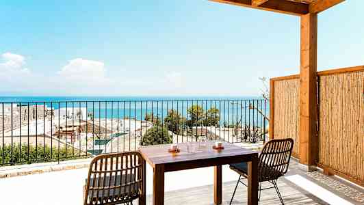 En terrasse med et træbord og stole, der vender mod en udsigt over havet. (AI-genereret tekst)