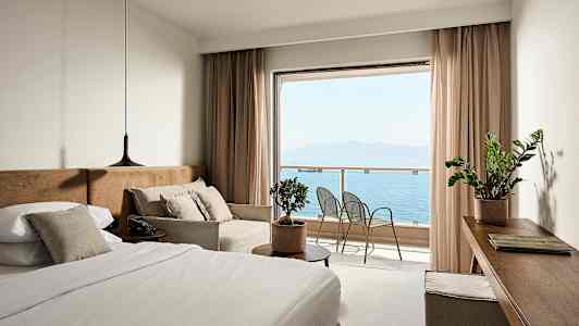 Et hotelværelse med en seng, sofa og udsigt over havet fra en balkon. (AI-genereret tekst)