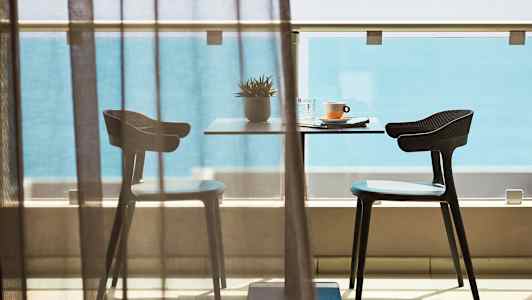 Et bord med to stole på en balkon foran havudsigt. (AI-genereret tekst)