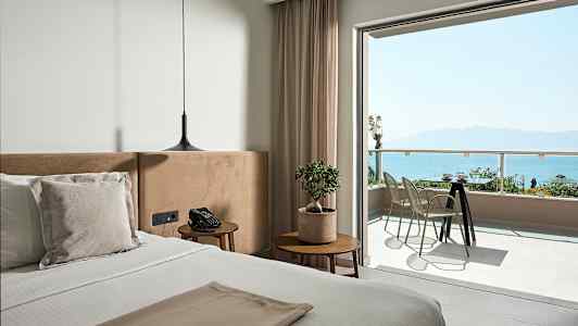 Et værelse med en seng, natbord, moderne hængelampe og en altan med udsigt over havet. (AI-genereret tekst)