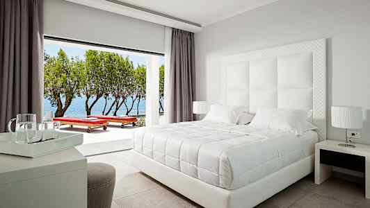 Et stilfuldt hotelværelse med en hvid dobbeltseng og udsigt over havet. (AI-genereret tekst)