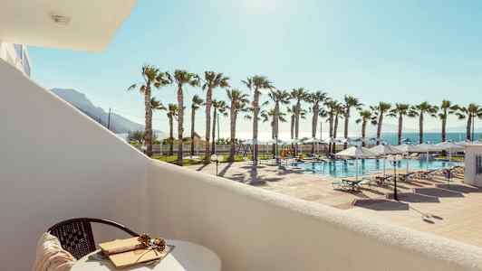 Udsigt fra en altan mod en pool med solvogne og palmer i solskin. (AI-genereret tekst)