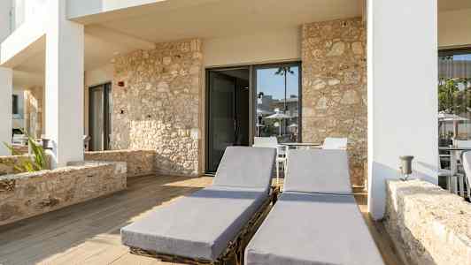 To solsenge på en stenbelagt terrasse foran bygning med stenfacade. (AI-genereret tekst)