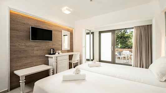 Et hotelværelse med to senge, skrivebord, tv og en terrasse med bord og stole synlige gennem glasdøre. (AI-genereret tekst)