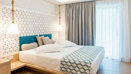 Hotelværelse med en dobbeltseng, stilren indretning og lyse gardiner. (AI-genereret tekst)